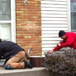 two pest control technicians sealing off exterior of home from mice entry